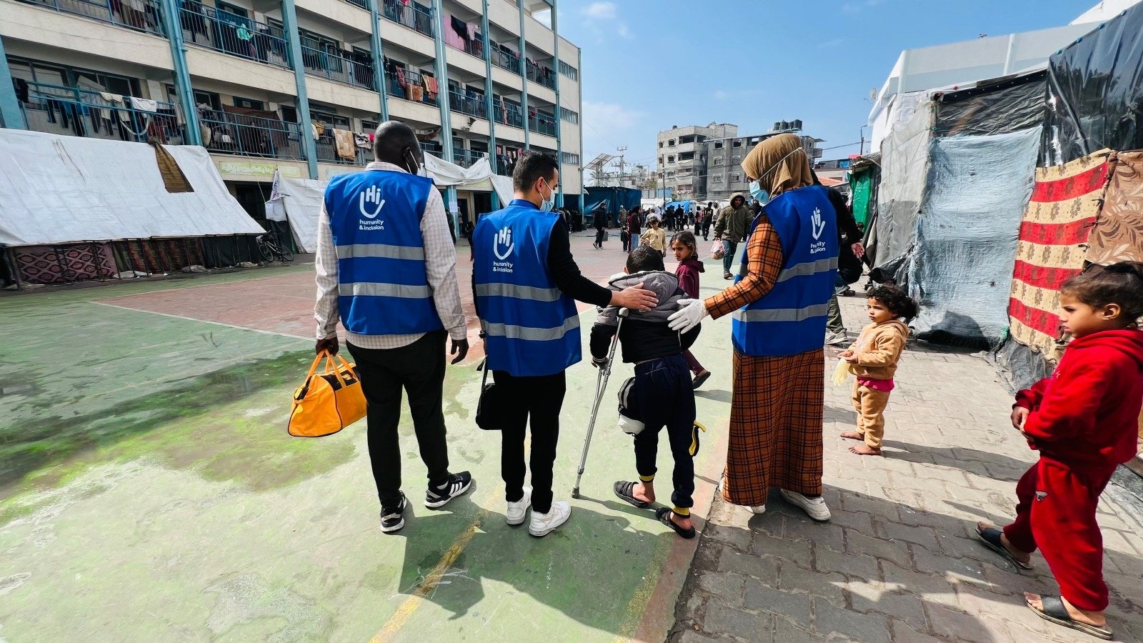 Un enfant est blessé à Gaza. Il est couché dans un lit avec une femme et un homme autour de lui. Son bras est dans un platre. 