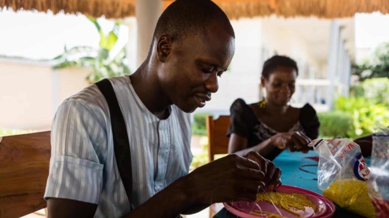 Perlenwerkstatt: Zwei Menschen basteln mit Perlen. Eine ergotherapeutische Maßnahme in Lomé