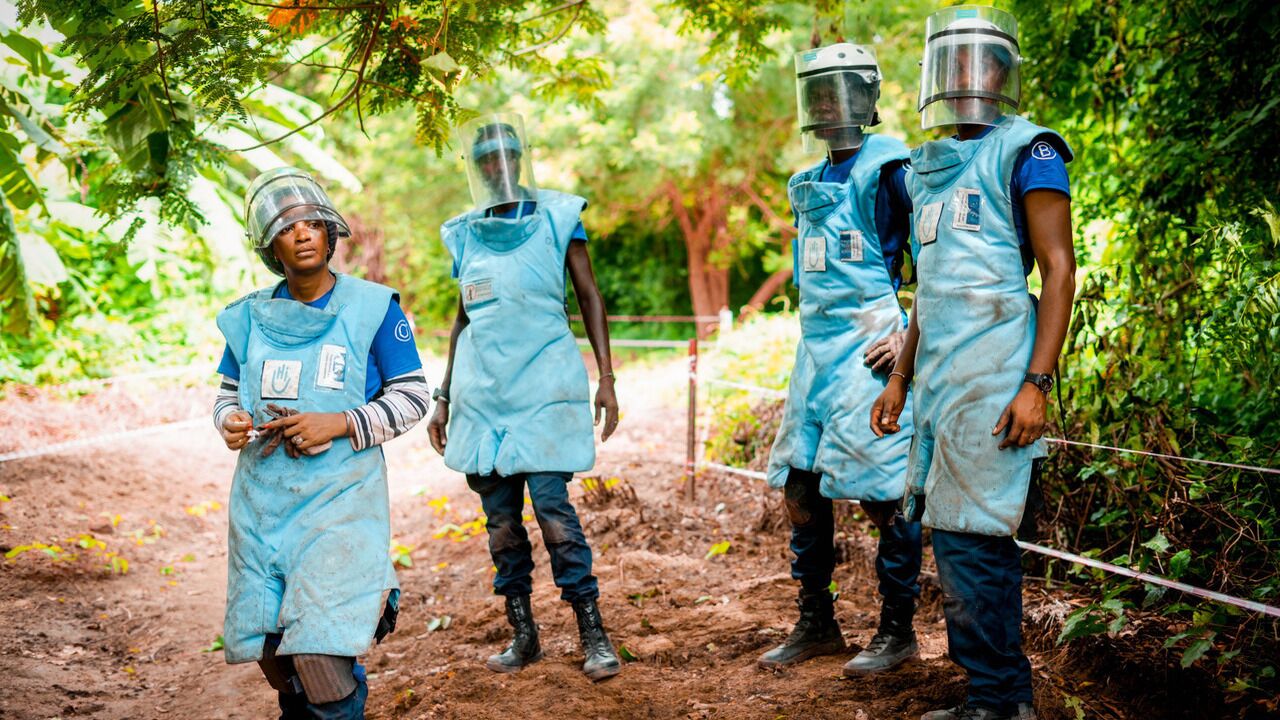 Eine Gruppe von vier Entminern und Entminerinnen bei der Arbeit. Sie tragen blaue Schutzkleidung und Helme mit Visier.