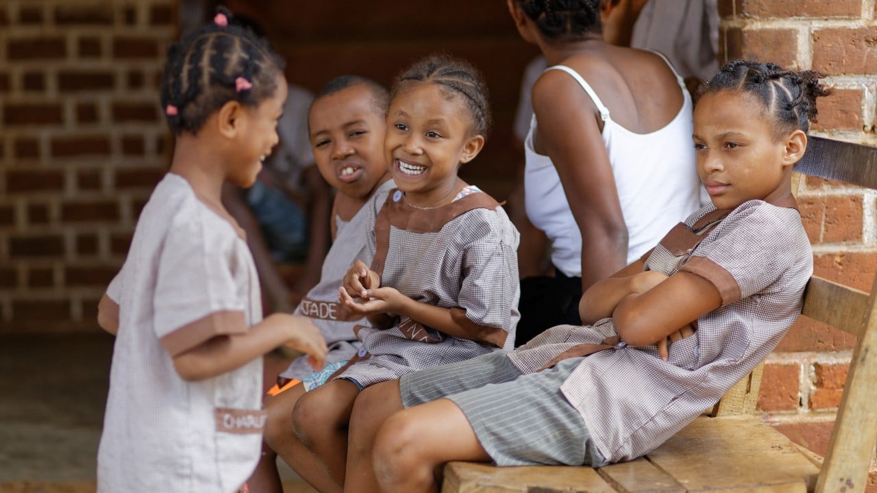 Plusieurs petites filles sont regroupées dans la cour de leur école, elles rient ensemble.