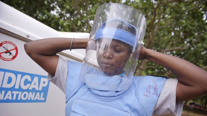 Fatou Diaw bei ihren Vorbereitungen für die Minenräumung. Bevor sie mit der Arbeit beginnt, zieht sie die Schutzausrüstung an und setzt ihren Helm auf Fatou Diaw bei ihren Vorbereitungen für die Minenräumung. Bevor sie mit der Arbeit beginnt, zieht sie die Schutzausrüstung an und setzt ihren Helm auf